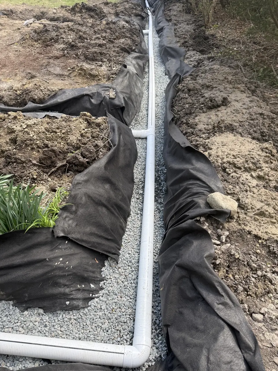 Perforated drainpipe laid in crushed stone and filter fabric for a French drain.