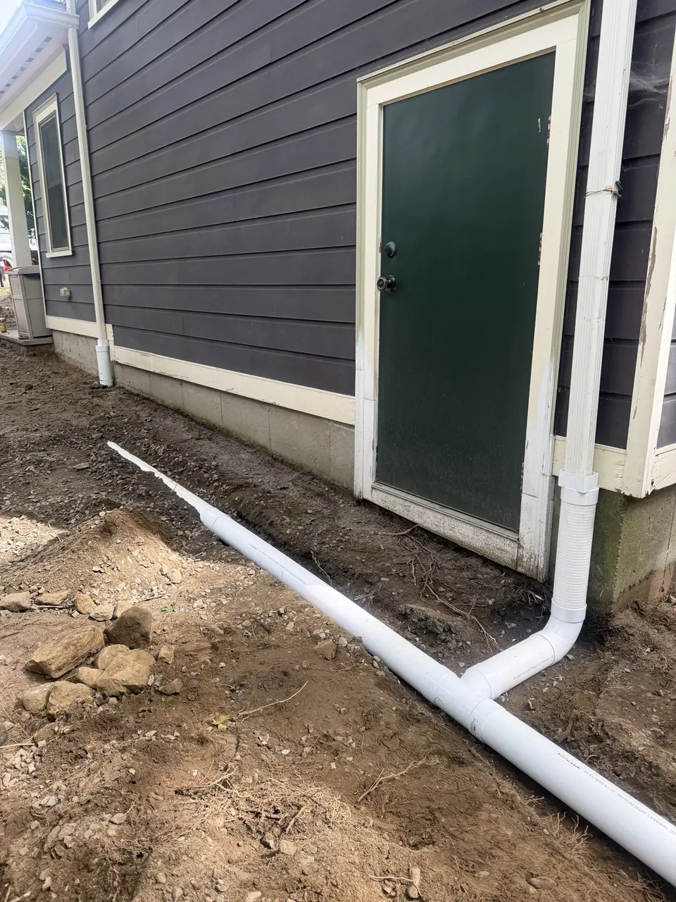 Downspout drainage pipes laid in a trench beside a home during installation.