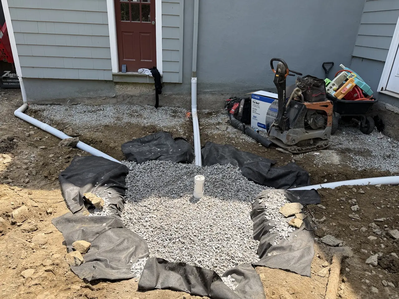 Crushed-stone dry well with connected downspout pipes during installation.