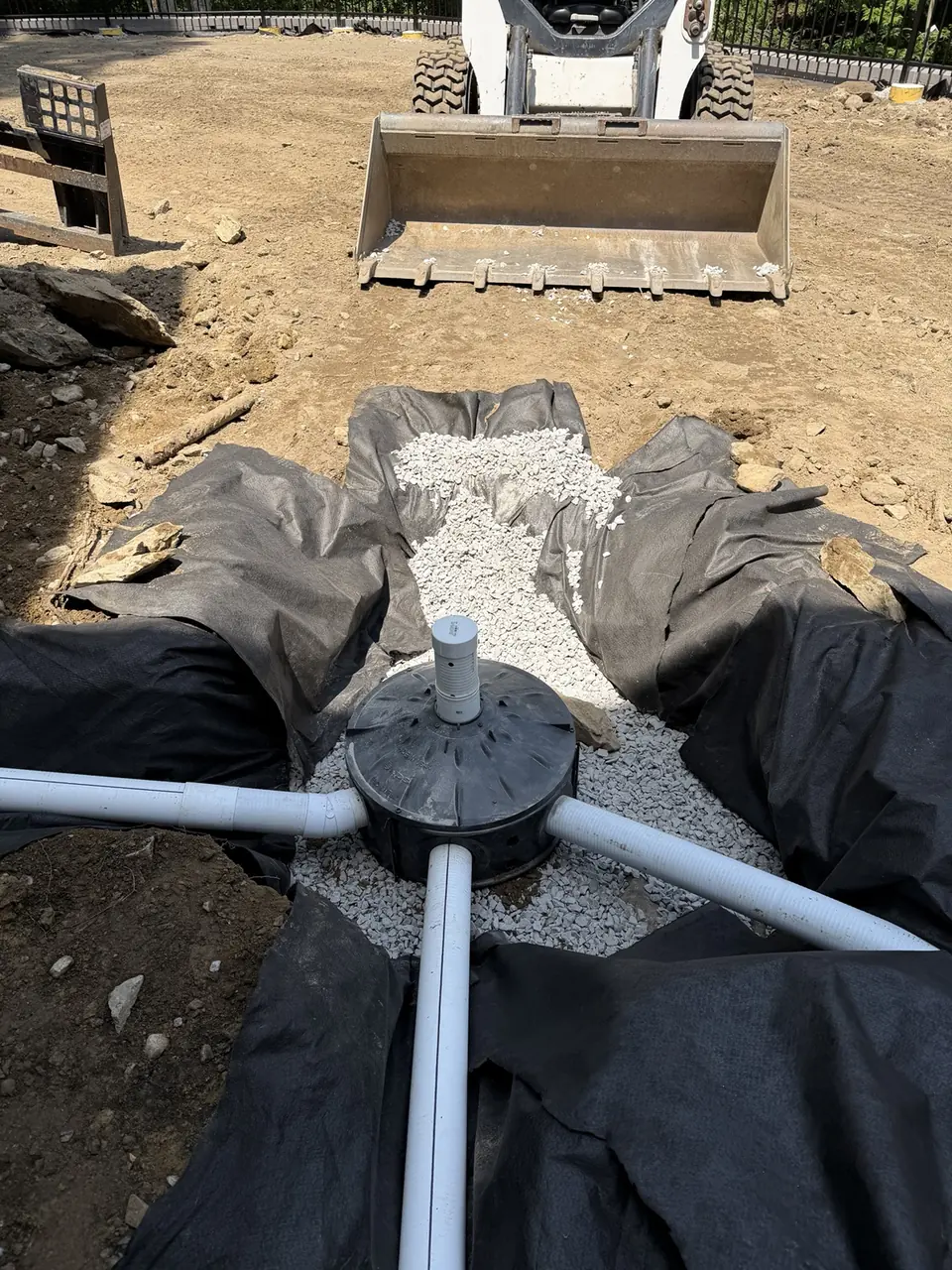 Underground drainage basin connected to pipes in a gravel-lined excavation.