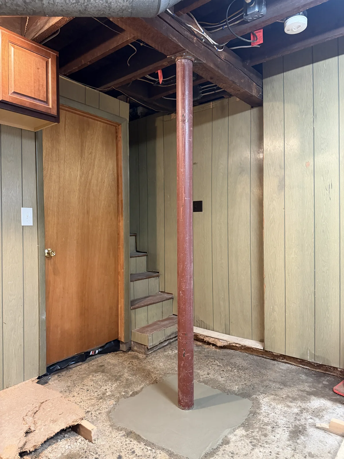 Installed Lally column beneath a wood beam with concrete patched around its base